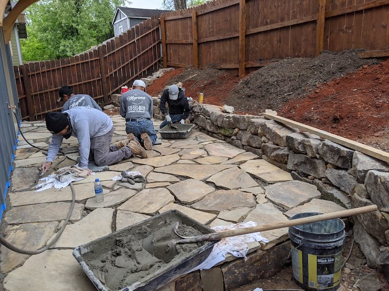 Four workers are laying stone outside a home.